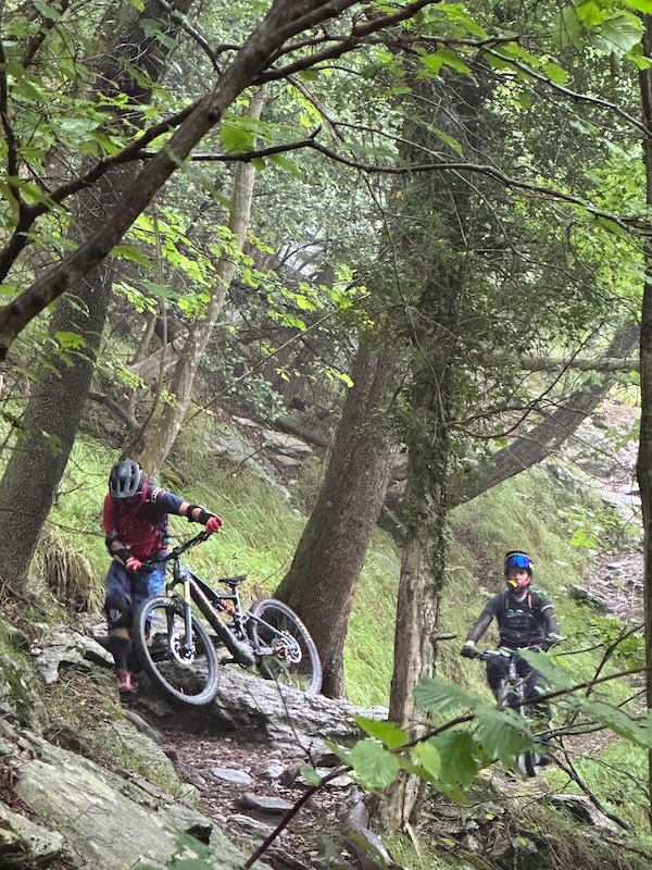 Behind another rider who is walking his bike over some slippery rocks