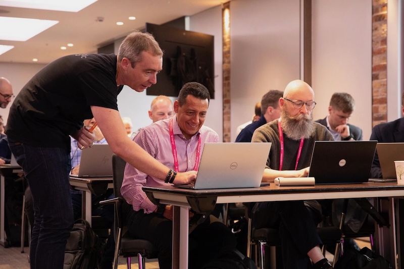 Lines of seated people working at laptops; I'm leaning over to help one person, who smiles as he gets it